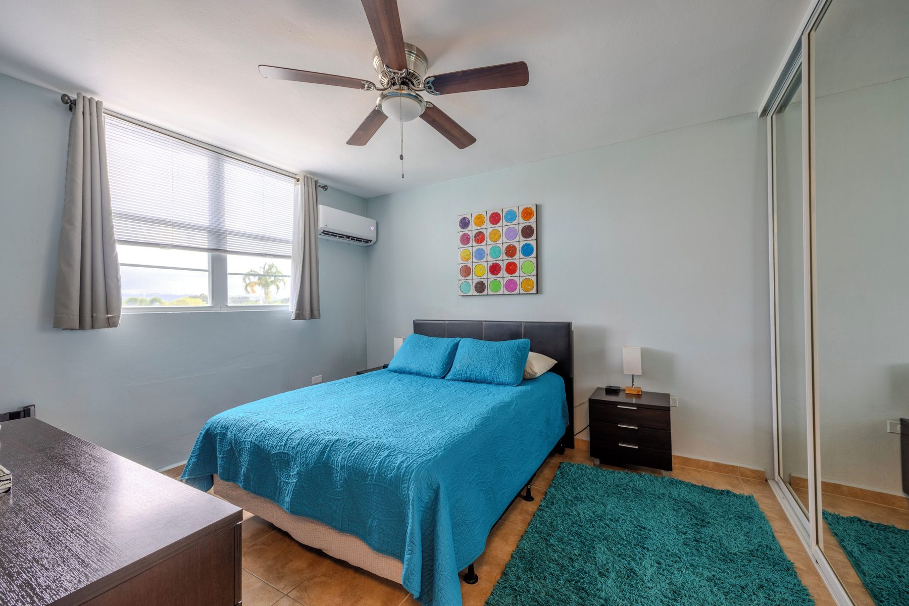 A second bedroom with a double bed, ceiling fan, ductless air conditioning, mirrored closet doors and a wide window