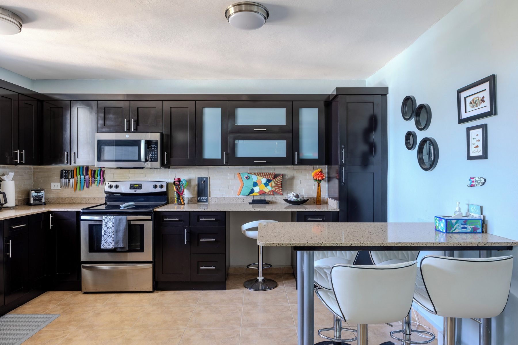 The kitchen with dark cabinets, stainless range and microwave, stone countertops and a breakfast bar with white stools