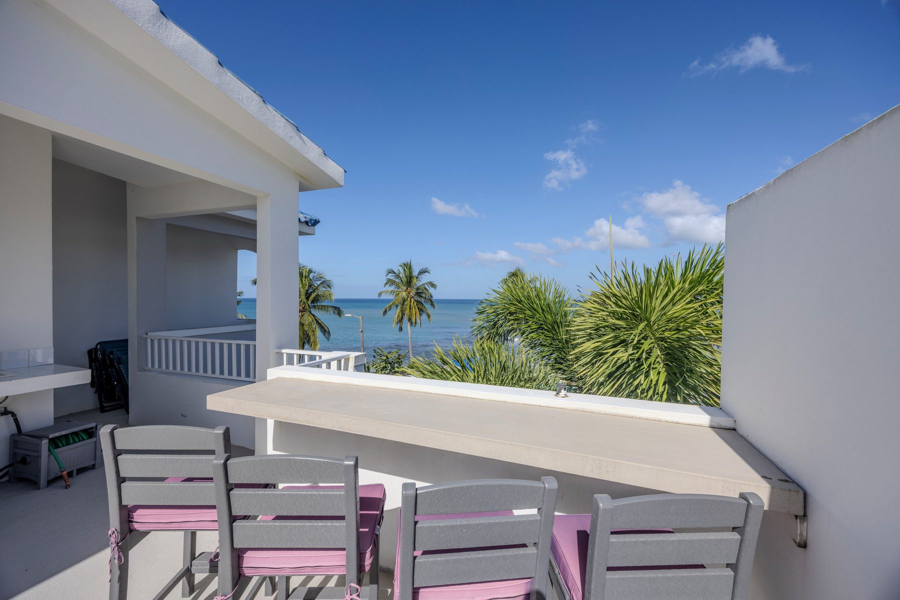 A long counter along the rooftop wall with four bar stools facing out toward palms and the ocean beyond